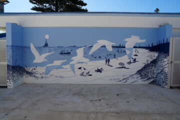 A mural depicting a beach scene with flying seagulls, people walking on the sand, boats on the water, and trees in the background, painted in shades of blue and white.