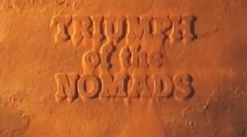 Text “TRIUMPH of the NOMADS” is engraved in a sandy, earth-toned textured background, resembling carved writing in a desert or ancient rock surface.