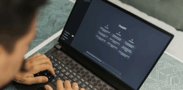 A person types on a laptop displaying the ChatGPT interface on the screen, with suggested conversation prompts visible. The laptop rests on a patterned surface.