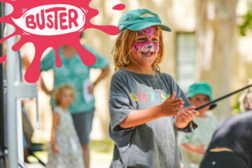 A smiling child with face paint resembling a pink cat stands outdoors, clapping hands. Other children are blurred in the background. The word BUSTER appears in a red splash graphic in the top left corner.