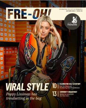 A woman in a colorful patterned outfit sits on a chair, leaning her head on her hand. She is surrounded by orange shoeboxes. The magazine cover headline reads “Viral Style: Poppy Lissiman has trendsetting in the bag.”.
