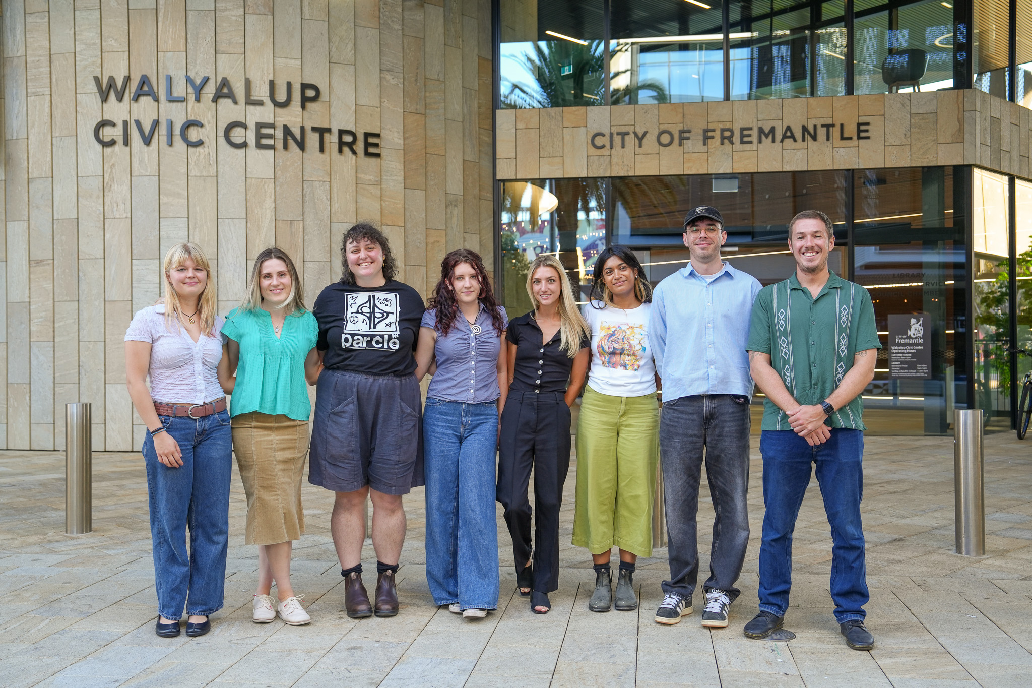 A group of nine people stand in a row, smiling, outside the Walyalup Civic Centre in Fremantle, with the building and its signage visible behind them.
