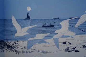 Illustrated scene of a beach with flying seagulls, a sailboat with a smiling sun in the background, people swimming and boating, and two empty chairs under a striped umbrella on the sand. The image is in shades of blue.