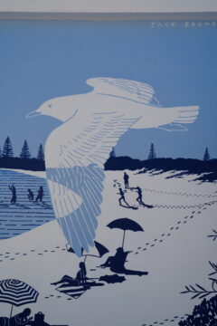 A mural depicting a large white bird flying over a beach scene with people swimming, walking, and sitting under umbrellas; blue and white tones dominate the artwork.