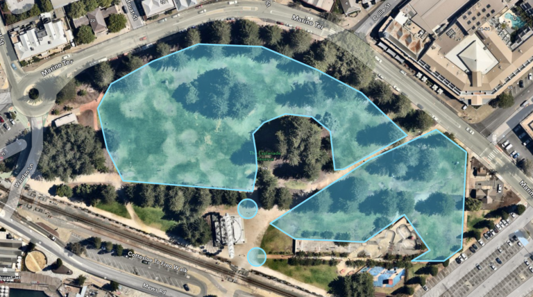 A satellite view of a city park with paths and trees. Two overlapping blue shapes outline areas within the park, and two blue circles are near a small white structure in the lower center. Streets border the park.