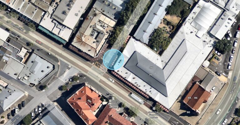Aerial view of an urban street with buildings, cars parked along the road, trees, and a blue circle highlighting a specific location on Milligan Street, near Murray Street, in a city area.