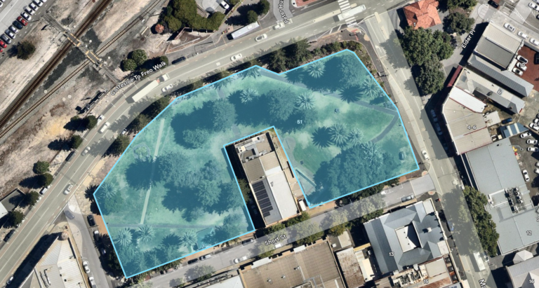 Aerial view of a city block with a park area highlighted in blue, surrounded by roads, buildings, and trees. The park has a central building and scattered palm trees.