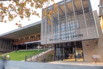 Modern glass and metal building with “Walyalup Civic Centre” sign at the entrance, surrounded by greenery and trees with autumn leaves. Steps and ramps lead to the main doors.