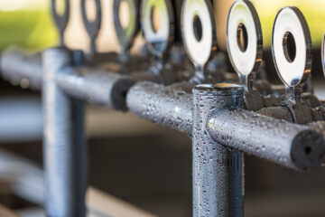 Close-up of metallic pipes covered in water droplets, with several round, reflective handles or taps aligned on top. The background is blurred, drawing focus to the textured, moist surfaces.