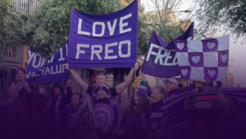 A group of people in purple clothing hold up banners reading LOVE FREO and FREO with hearts, showing support in what appears to be a public outdoor event.