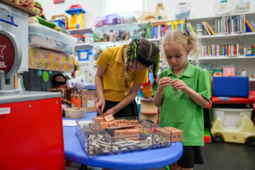 Two young girls in school uniforms building with a construction set at a table in a classroom.