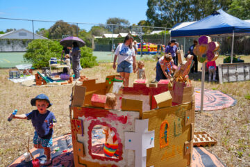 Children playing with cardboard structures and crafts at an outdoor event on a sunny day.