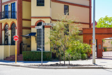 A street sign at the corner of Henry Street and Marine Terrace next to a no entry sign, in front of a tan and red brick building.