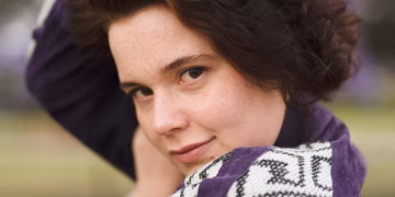 A person with dark hair and freckles looking toward the camera.