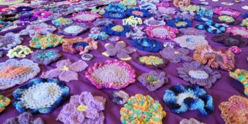 A purple fabric surface covered with a variety of colorful, hand-crocheted floral appliques.