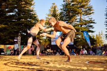 Two Indigenous Australian men performing a traditional dance on sand, their bodies decorated with white ochre.